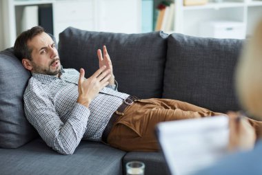 Genç ve rahat bir adam danışman ile konuşurken kanepede uzanıyor ve bireysel seans sırasında sorununu anlatıyor.