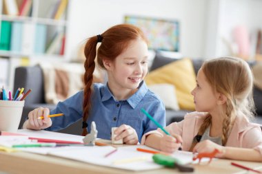 Sıcak güneş ışığı ile aydınlatılan evde masada otururken birlikte resim çizerken birbirlerine bakan iki kız kardeş portresi, kopya alanı