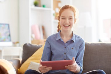 Waist up portrait of red haired teenage girl smiling at camera while using digital tablet in sunlight, copy space clipart