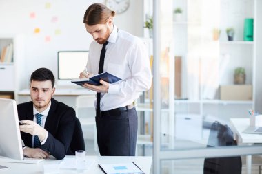 Meslektaşı bilgisayar monitöründeki çevrimiçi verileri işaret ederken not defterine not alan genç brokerlardan biri