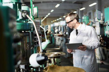 Üst düzey kalite müfettişin yan görünüm portre fabrika atölyesinde endüstriyel makine üniteleri kontrol laboratuar ceket giyiyor, kopya alanı