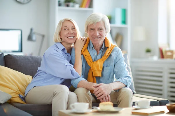 Portrait of happy mature couple posing together sitting on sofa at home, copy space