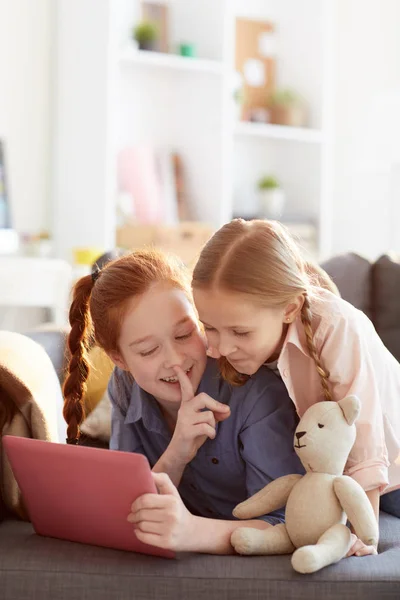 Retrato Duas Meninas Felizes Sussurrando Secretamente Usar Tablet Digital Deitado — Fotografia de Stock
