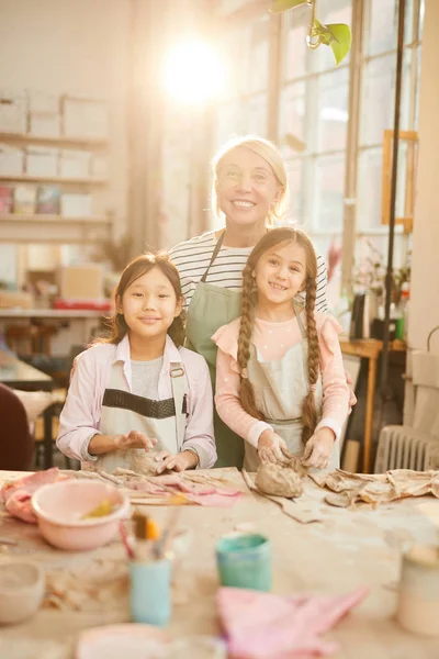 Çömlekçilik sınıfında iki küçük kız ile poz gülümseyen sanat öğretmeni portresi, sahne güneş ışığı ile aydınlatılmış