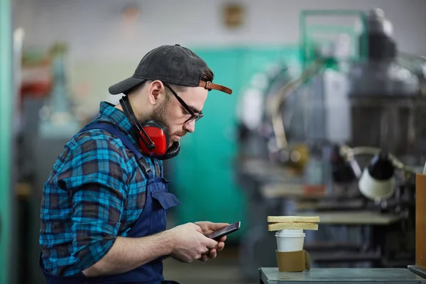 工場でのコーヒーブレイク中にスマートフォンを使用して作業者の側面図ポートレート コピースペース — ストック写真