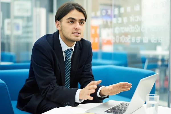 Portrait of Middle-eastern businessman gesturing actively while using laptop in office, copy space