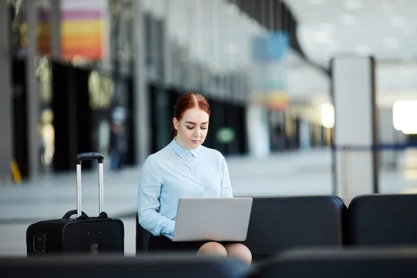 Portrait of young businesswoman using laptop while waiting in airport lobby, copy space