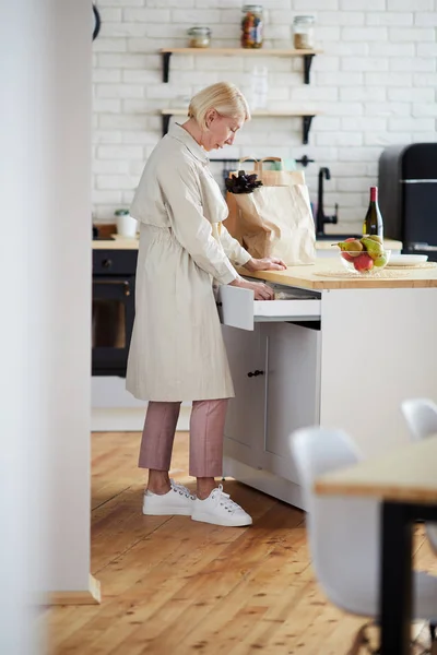 Serious Stylish Mature Woman Coat Standing Kitchen Counter Finding Utensil — Stock Photo, Image