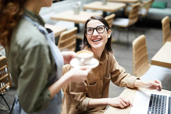 カフェでウェイトレスと話しながら テーブルに座ってラップトップを使用して メガネで陽気な興奮したビジネスウーマン — ストック写真