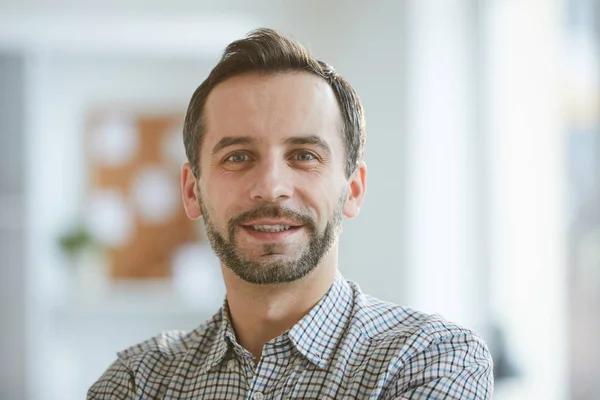 Happy and successful professional in casual shirt looking at you while standing in front of camers in office