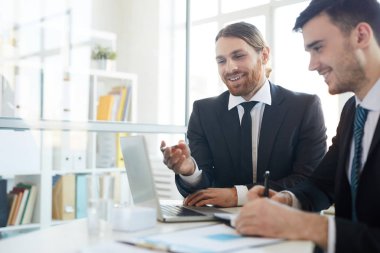 Yeni iş stratejilerinin sunum yaparken dizüstü bilgisayar ekran ını işaret eden neşeli başarılı brokerlardan biri