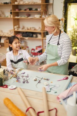 Küçük Asyalı kız ile çiçek kompozisyonları oluşturma gülümseyen olgun kadın yüksek açılı portre, uzay kopyalamak