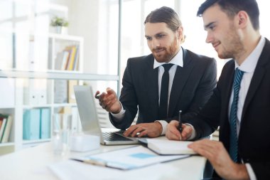 Yanında notlar yaparken dizüstü bilgisayar ekranını işaret eden genç zarif analistlerden biri