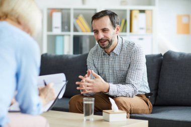 Genç adam, danışmanın önünde kanepede oturuyor ve ona ofiste yaşadığı sorunları anlatıyor.