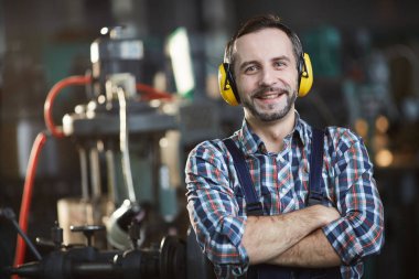 Bel kadar sakallı fabrika işçisi kolları ile atölye ayakta poz earmuffs giyen portre, kopya alanı