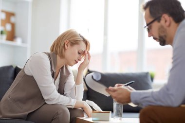 Psikolojik danışma sırasında kanepede otururken alnına dokunan yorgun ve stresli kadın
