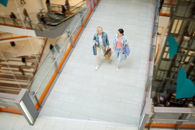 Alışveriş para harcama sırasında bahar satışı ve alışveriş merkezi üzerinde yürüyüş tartışırken rahat giyim neşeli olgun ve genç bayanlar üst görünümü