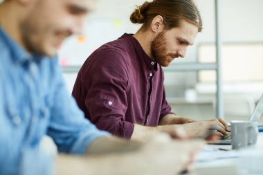 Bir genç rahat ofis yöneticileri dizüstü önünde oturan ve net sörf yaparken tuşlarına basarak