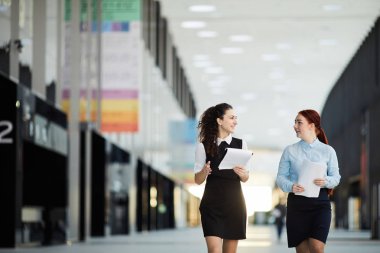 Ofis salonunda kameraya doğru yürüyen iki genç iş kadınının portresi, kopya alanı