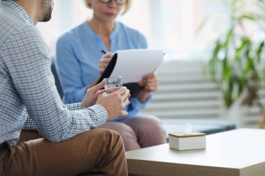 Pschologist yanında kanepede oturan ve hikayesini anlatan su bardağı ile sorunlu adam