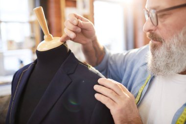 Gözlüklü sakallı kıdemli terzi terzi dükkanında çalışırken sarı iplikleri ile kukla yeni ceket dikiş