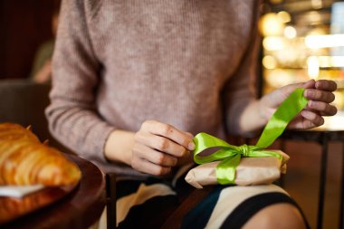 Genç kadının elleri, kafede otururken hediyeye bakmak için paketin üzerine ipek yeşili kurdele yitirme