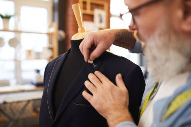 Terzilik mağazasında müşteri sırası üzerinde çalışırken ceket üzerinde ilik için kıdemli terzi çizim hattı