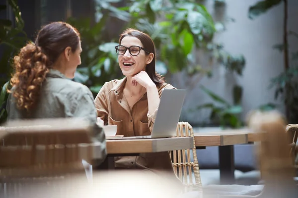 戴着眼镜的兴奋的年轻女子坐在桌旁 与同事共进午餐时大笑 — 图库照片