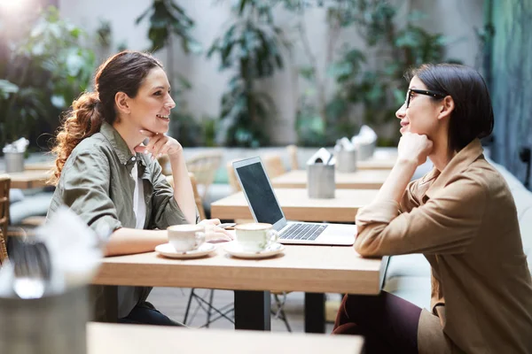 积极自信的商务女士穿着休闲衬衫坐在咖啡馆的桌子旁 讨论项目和计划 她们使用笔记本电脑 — 图库照片