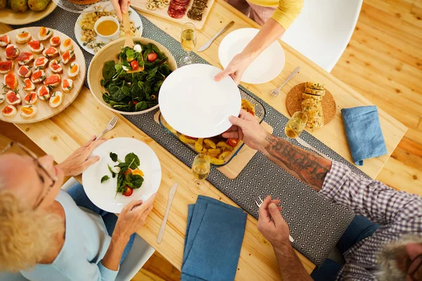 夕食中にサラダを入れて彼女に頼んでいる間に女性にプレートを与える腕にタトゥーを持つ男性の高アングルビュー — ストック写真