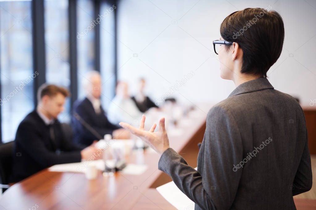 Back view portrait of young businesswoman giving speech in conference room and gesturing, copy space