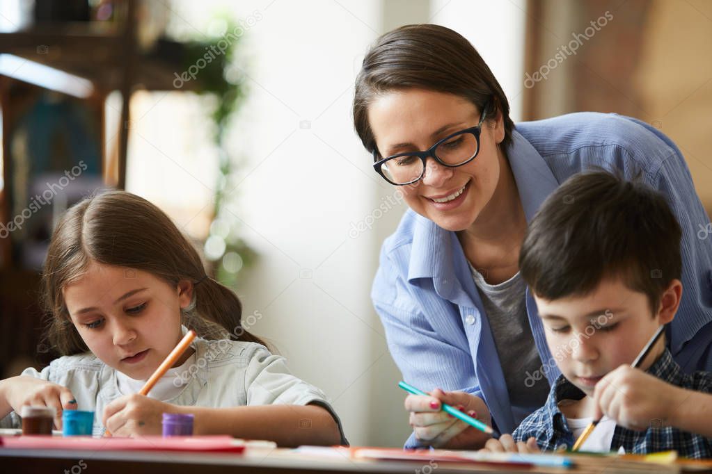 Portrait of happy modern woman helping two kids drawing pictures at home, copy space