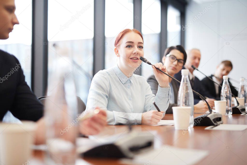 Portrait of smiling young businesswoman speaking to microphone during press conference or training seminar, copy space