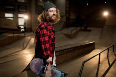 Uzun saçlı adam elinde kaykay tutan bel ekstrem spor parkı ayakta kamera bakarak, flaş ile vuruldu