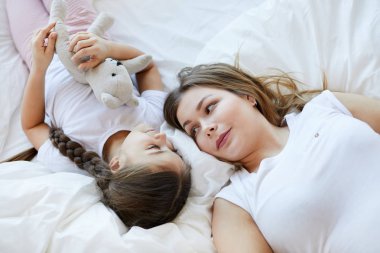 Beyaz çarşaf üzerinde sevimli küçük kız ile yatakta yatan genç anne portresi yukarıda, kopya alanı