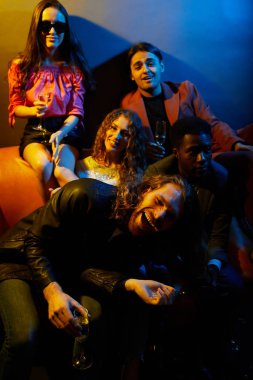 Neşeli güzel şık gençlerin bir grup kanepede oturan ve partide şampanya içme