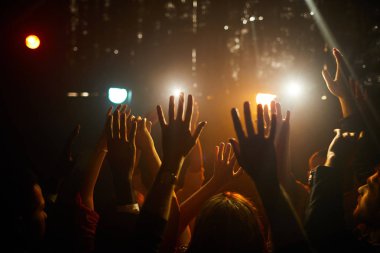 Karanlık kulüpte duran ve sahnede sanatçı beklerken havada el sallayarak tanınmayan insanların kalabalık