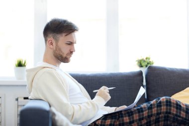 Kanepede döşeme çalışma belge tutan yakışıklı genç adamın yan görünüm portresi, kopya alanı