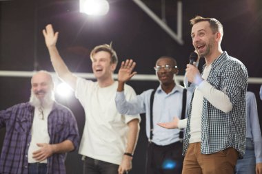 Heyecanlı olgun adam portresi arka planda sallayarak insanlarla sahnede mikrofona konuşan, kopya alanı