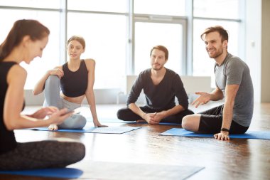 Doğal ışık dolu odada yerde oturan ve seminerde yoga öğretmeniyle konuşan pozitif meraklı genç öğrencilerden oluşan bir grup