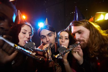 Arkadaşlar sürpriz parti yapma: parti kapakları neşeli gençlerin bir grup daireler içinde duran ve karanlık odada parti boynuzları üfleme