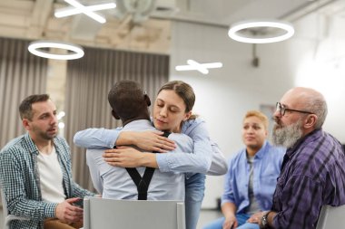 Destek grubunda terapi oturumu sırasında Afrikalı adama sarılan karışık genç kadının portresi, kopya alanı