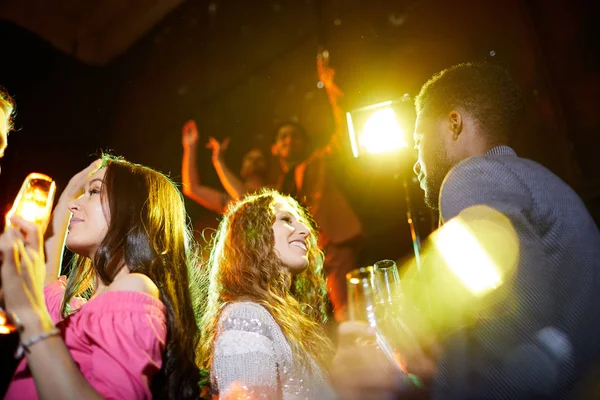 Positive carefree young people drinking alcohol and chatting at hilarious party in contemporary nightclub