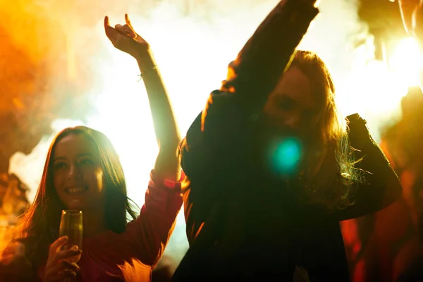 Cheerful energetic young people dancing in smoke and waving hands while having fun in nightclub