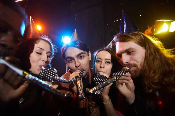 Arkadaşlar sürpriz parti yapma: parti kapakları neşeli gençlerin bir grup daireler içinde duran ve karanlık odada parti boynuzları üfleme