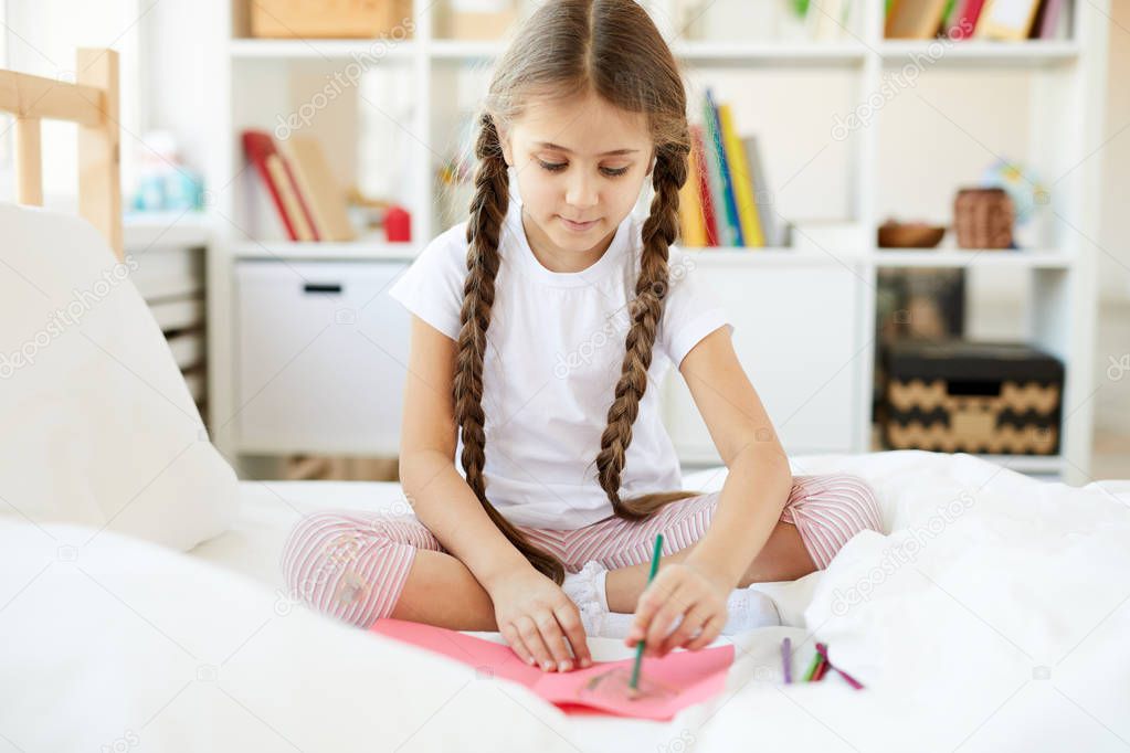 Portrait of cute little girl drawing pictures sitting on bed in cozy childrens room, copy space