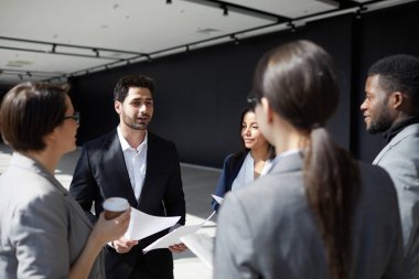 Daire içinde duran formalwear içerik yaratıcı modern iş arkadaşları grubu: karma ırk profesyonel meslektaşlarına yeni proje hakkında bilgi ile kağıtları gösteren