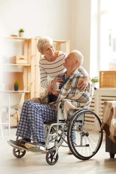 Full length portrait of senior woman caring for husband sitting in wheelchair, copy space