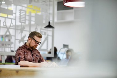 Sakallı ve bıyıklı ciddi meşgul öğrenci adam kütüphanede masada oturan ve bilimsel makaleler üzerinde çalışırken notlar yapma