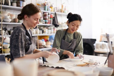 Atölyede zanaat araçları ve kum kağıtları ile işleme yemekleri ile masada oturan önlük pozitif çekici genç çok ırklı kadınlar